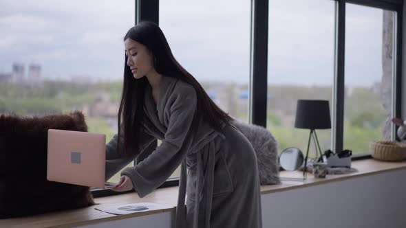 Portrait of Slim Confident Beautiful Asian Woman Taking Laptop Sitting Down on Windowsill and