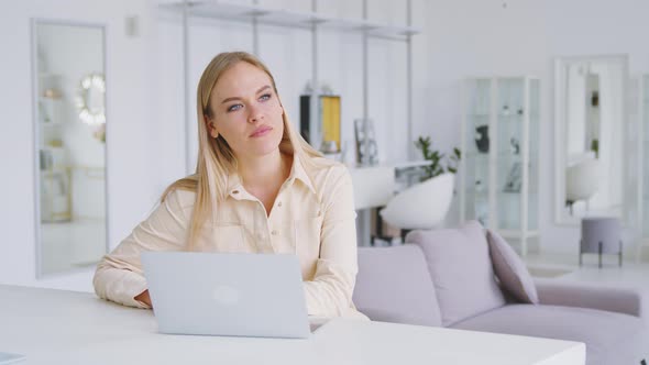 Thinking girl at the desk with a laptop in a white room