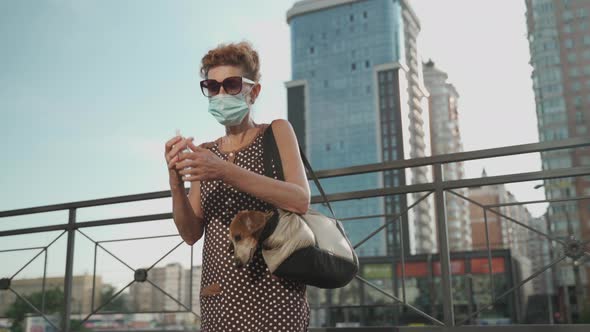 An Elderly Dog Owner in a Medical Mask Uses an Antiseptic While Walking in the City