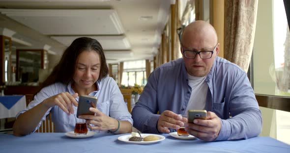 Brunette Woman Is Browsing By Smartphone in Cafe and Chatting with Her Husband