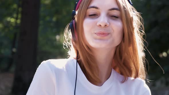 Portrait of Pretty Positive Teenage Girl with Red Hair Listening to Music in Pink Earphones Smiling
