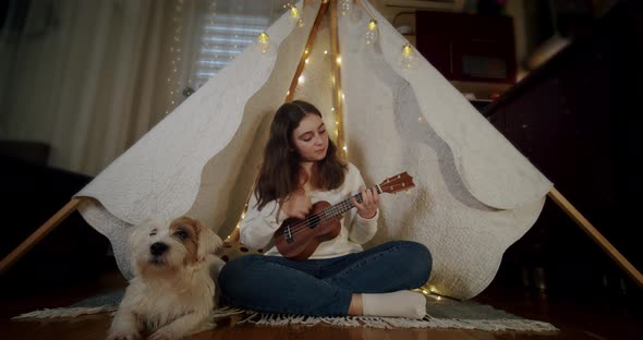 The Girl Sits in a Children's Tent with a Dog Jack Russell and Plays the Guitar