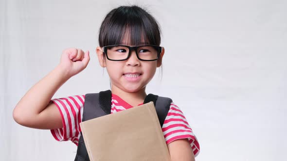 Smiling schoolgirl wearing summer outfit with backpack holding books on white background in studio.