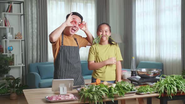 Asian Young Dad And Daughter Make Funny Faces With Vegetable Cooking Together In Home