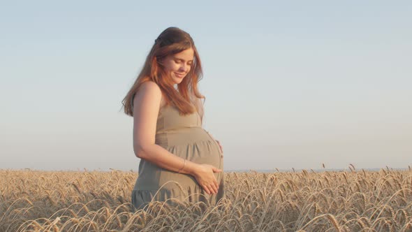 Pregnant happy red-haired woman touching her belly, future young mother walking at sunset