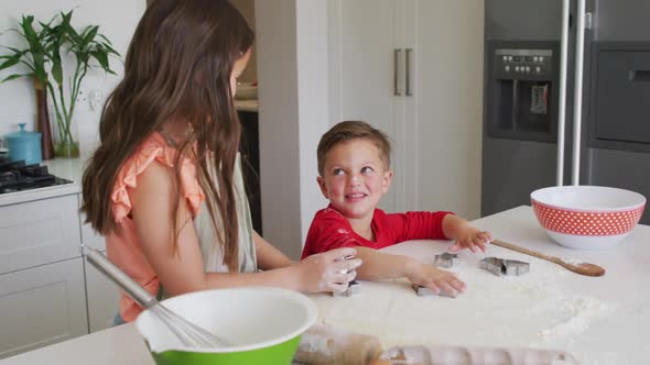 Happy caucasian siblings baking together, preparing cookies in kitchen