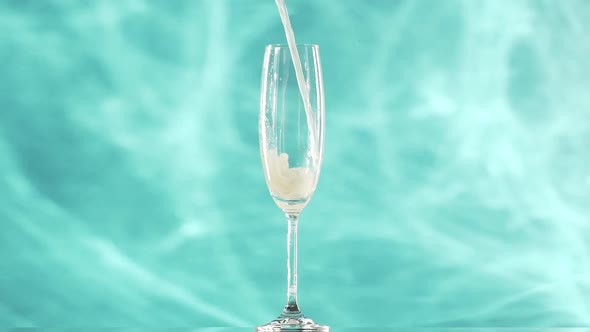 Yellow Soda Water is Pouring Into Champagne Flute Glass Standing Over Smoky Cyan Background