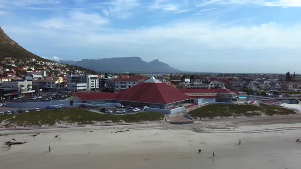 Drone shot of Muizenberg beach, Cape Town - drone is reversing from a house, revealing the beach and