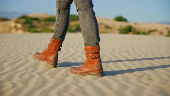 Woman's legs in hiking boots walking on the sand in the desert