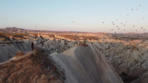 Brunnette girl whatching the sunrise in Cappadocia under a sky of colorful balloons. Turkey.