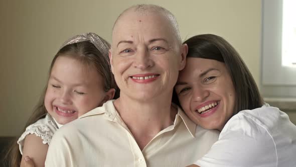 An Adult Daughter and Little Granddaughter Hug a Sad Elderly Woman Who Has Gone Bald After