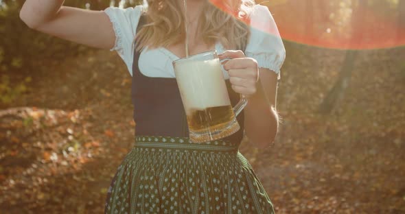 Slavic Wife in National Costume Pours Beer Into a Mug at Lush Breasts in Forest