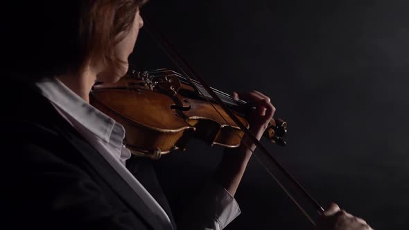 Dark Studio Where a Musician Plays the Violin While Standing with His Back. Black Smoke Background