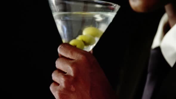 Androgynous man drinking cocktail against black background