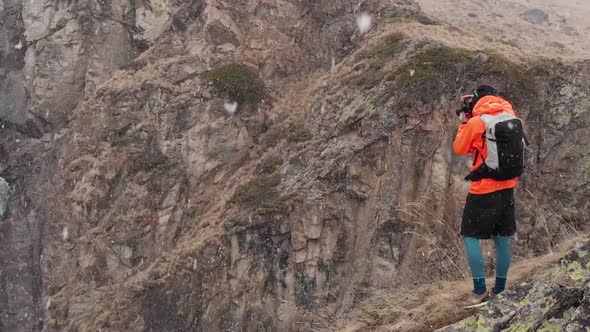 Aerial View of a Young Male Photographer with a Camera in His Hands Stands on a High Rock in a Gorge