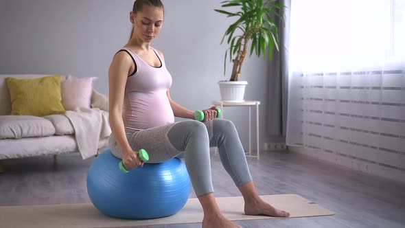 Pregnant Woman Doing Dumbbell Exercise and Sitting on Ball in Home Room Spbd