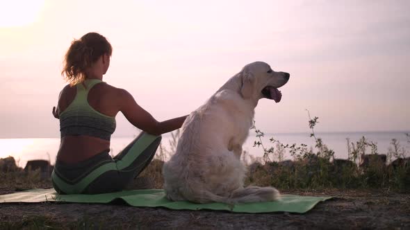 Fit Woman Meditating Sitting Next To Dog on Shore