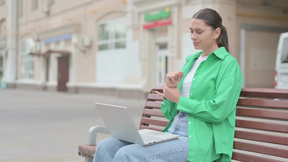 Hispanic Woman with Wrist Pain Using Laptop While Sitting on Bench