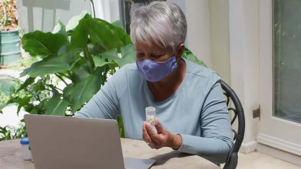 Senior mixed race woman wearing face mask having medical consultation using laptop