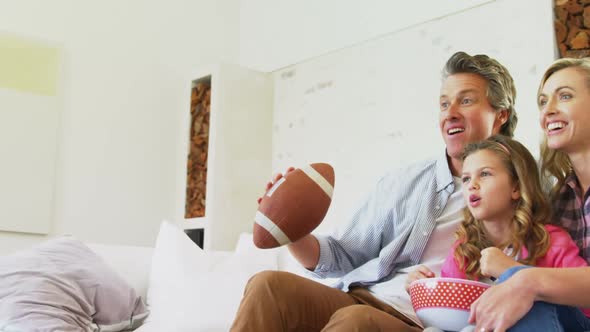 Smiling family watching television while having popcorn in living room 4k