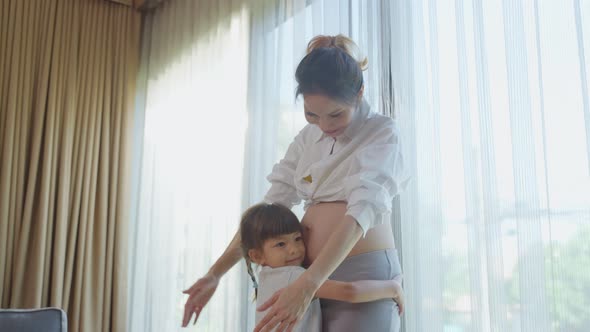 Asian young daughter hug and stroking beautiful pregnant mother tummy.