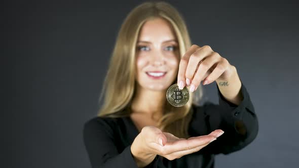 Young blonde woman shows a bitcoin coin,drops it in her open hand.