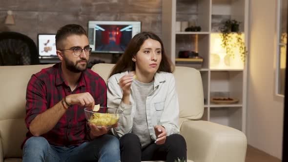 Caucasian Young Couple Eating Chips While Watching TV