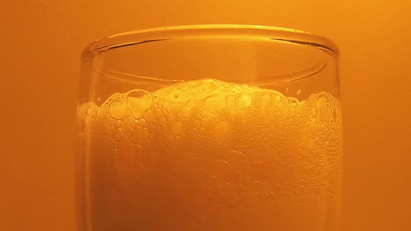 Close up of beer foam in glass against orange background. Static