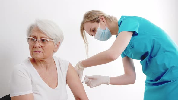 Scared Elderly Grayhaired Grandmother in a White Tshirt is Getting Vaccinated By Healthcare