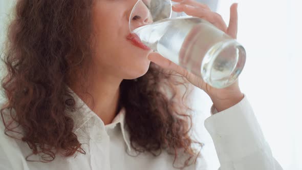 Close up of Latino woman sit on bed, hold a glass of water in bedroom.