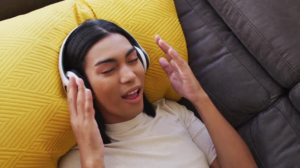 Gender fluid male wearing headphones enjoying listening to music while lying on the couch at home