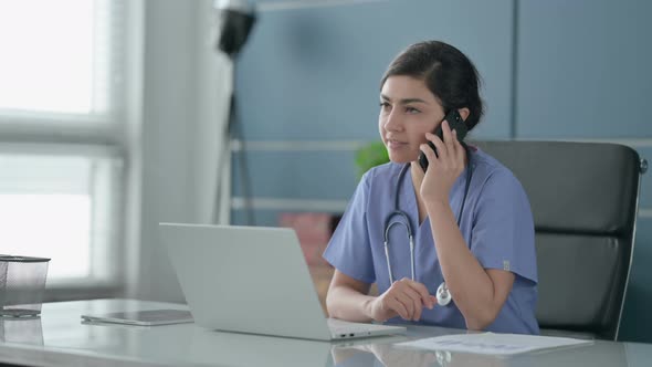 Indian Female Doctor Talking on Smartphone while using Laptop in Office