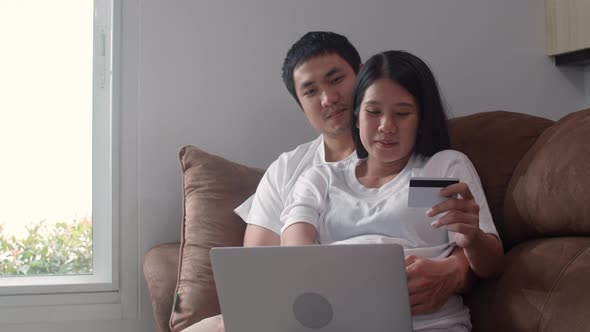 Young Asian Pregnant couple online shopping feeling happy using laptop credit card buy baby product
