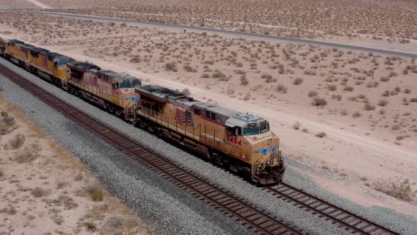 A freight train moves across the desert from a high angle.