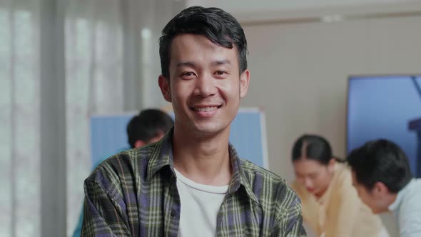 Smiling Asian Man Engineer Crossing His Arms To Camera While His Colleagues Are Working