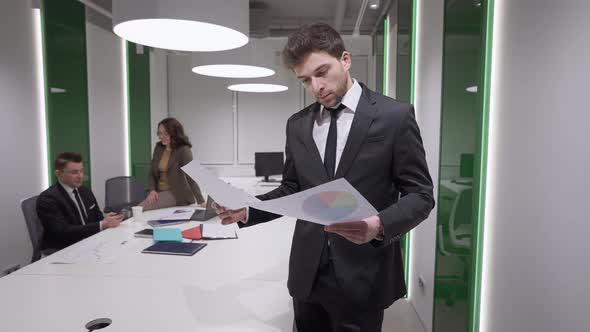 Portrait of Handsome Professional Male Analyst Standing with Paperwork in Office Turning Looking at