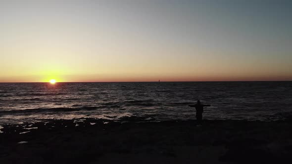 Black Dark Silhouette of Person Standing on A Beach with Arms Wide Open Looking Towards Sunset