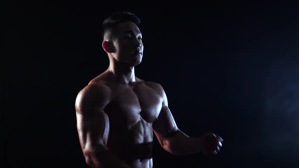 Asian Bodybuilder Demonstrates the Inflated Body, He Is Strong, Black Background, Slow Motion