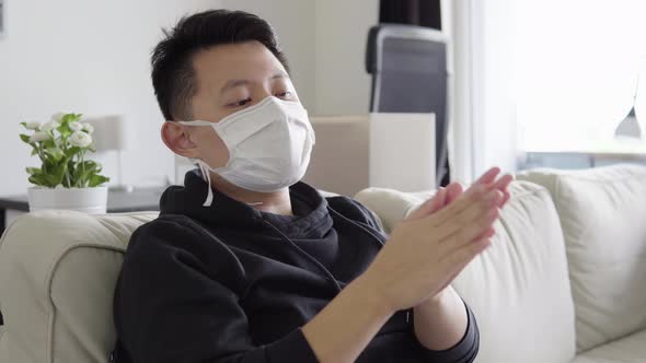 A Young Asian Man in a Face Mask Applies Disinfection Gel on His Hands and Looks at the Camera