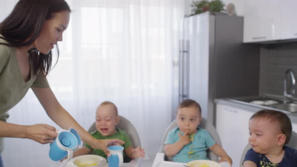 Young Mom Giving Sippy Cups to Messy Baby Triplets