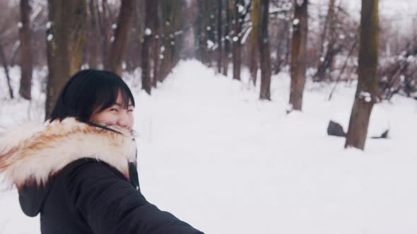 Portrait of Young Asian Woman Leading Her Boyfriend Into the Park Covered in Snow