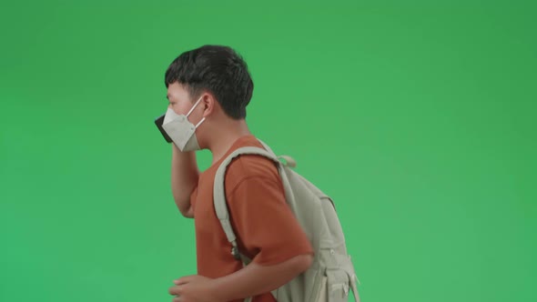 Asian Boy Student Wearing A Mask, Talking On The Phone While Running To School On Green Screen