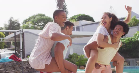 Two happy diverse male friends holding piggyback female friends in backyard at pool party