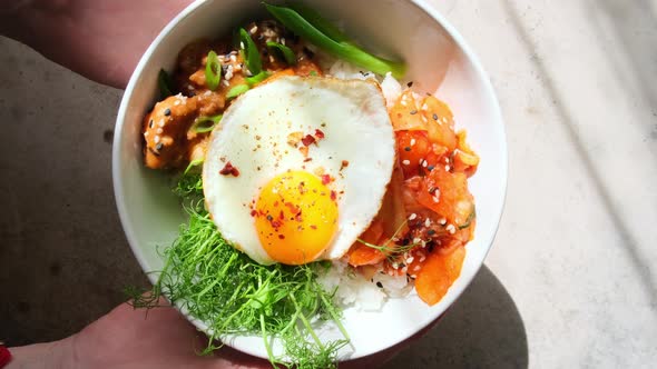 Bibimbap - meat, rice, kimchi, egg and sprouts in white bowl.