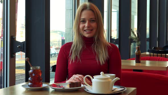 A Young Attractive Woman Sits at a Table with Meal in a Cafe and Talks To the Camera with a Smile