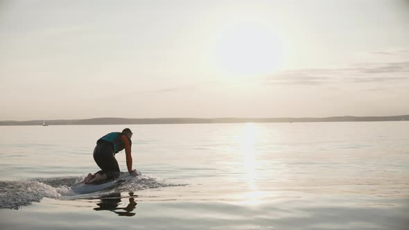 Man Riding a Hydrofoil Surfboard on Large Lake at Golden Sunset Sitting on Knees