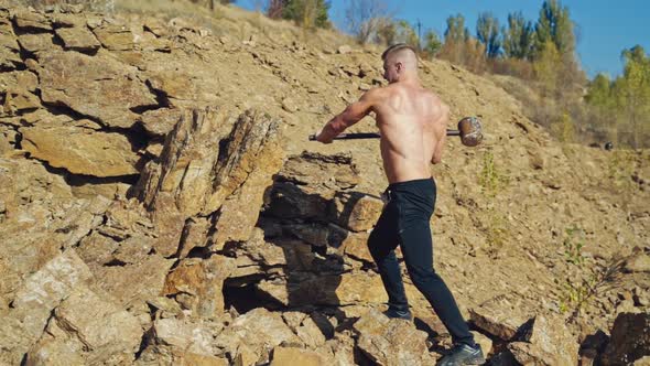 Shirtless bodybuilder splitting rocks with a sledgehammer