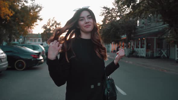 Young Girl in Stylish Black Clothes Goes Along the Road of the Autumn City and Turns to the Camera