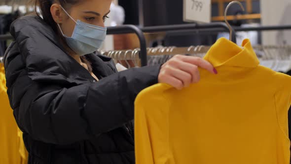 Young Woman in Disposable Mask Holds Yellow Pullover