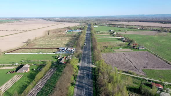 Aerial view of cars driving along the empty roadriding along trees and field